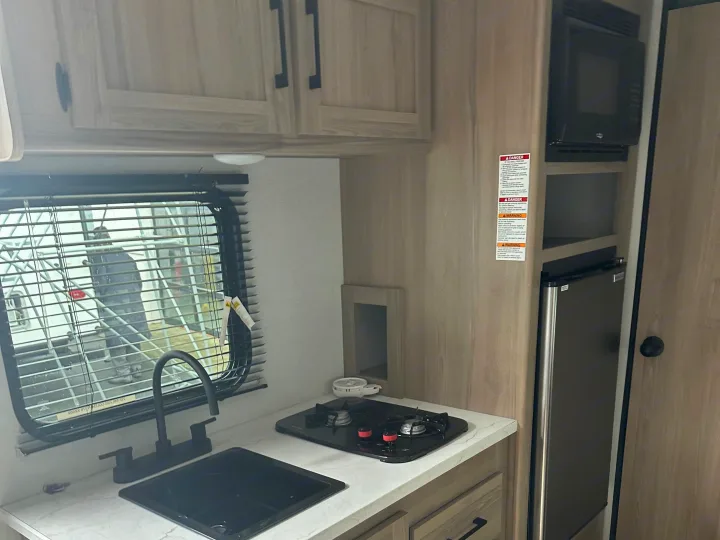 RV rental: A compact kitchen with light wood cabinets, black sink, two-burner gas stove, microwave, and refrigerator for convenience.. Coleman 17B 2025