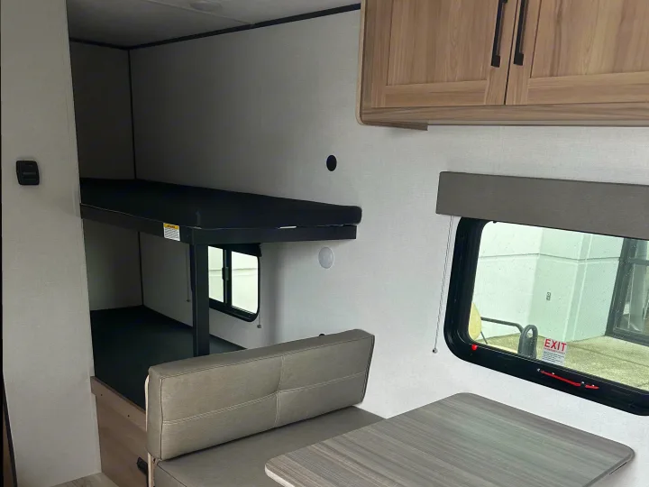 Inside an rv rental, featuring bunk beds, a dinette with table and bench, and overhead cabinets for storage.. Coleman 17B 2025