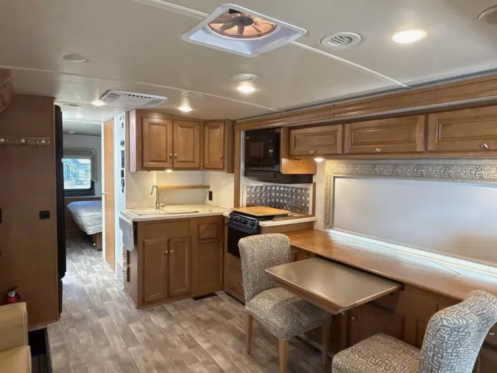 Inside this modern rv rental, admire the well-equipped kitchen, dining space, and a cozy bedroom in the distance. Ready for travel!. Winnebago Vista LX 2017