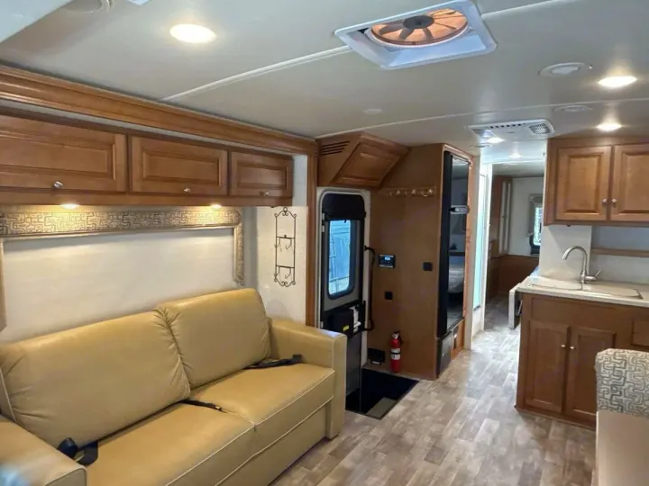 RV rental interior: cozy living area with beige sofa, overhead cabinets, kitchen sink, and wood-look floor.. Winnebago Vista LX 2017