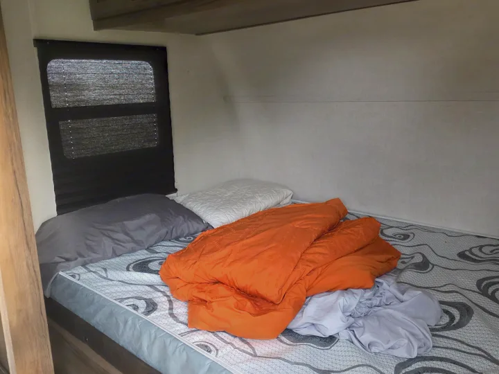 Cozy RV rental bedroom with a bed, orange comforter, pillows, and window blinds.. Avenger LT 2021