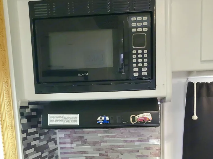 Rv rental kitchen featuring a compact black microwave, gas stove/oven, and modern tiled backsplash.. CoachMen Freelander 2012