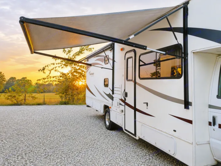 An RV rental with an extended awning catches the golden sunset light, parked on gravel, ready for adventure.. CoachMen Freelander 2012