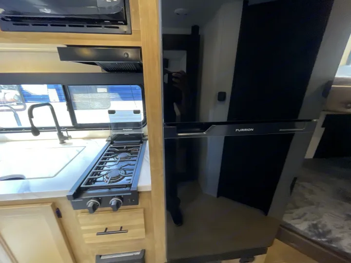 Functional RV rental kitchen with a black Furrion refrigerator, two-burner stove, sink, microwave & range hood.. Forest River Cherokee Wolf Pup 2026