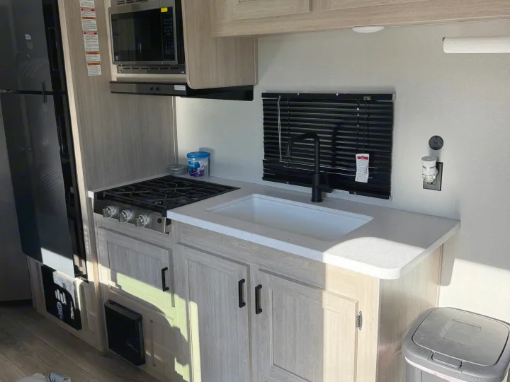 Modern RV rental kitchen with light wood cabinets, featuring a stove, sink, refrigerator, microwave, and functional countertop.. Coachmen Catalina 261 bh 2026