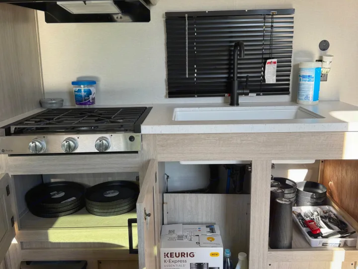Modern RV rental kitchen showcasing a GE Profile stove, sink, black blinds, and open storage with dishes, Keurig, and essentials.. Coachmen Catalina 261 bh 2026