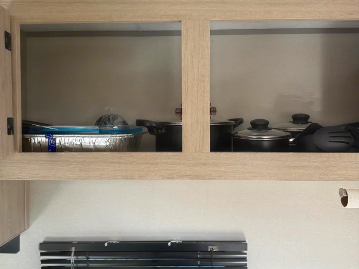 Inside an rv rental kitchen cabinet: pots, pans, cooking utensils, and a foil pan with a blue lid. Compact storage.. Coachmen Catalina 261 bh 2026