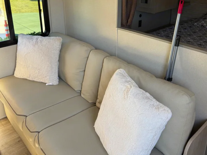 RV rental living space: Light-colored sofa with fluffy white cushions, a window, and view of the bed area.. Coachmen Catalina 261 bh 2026