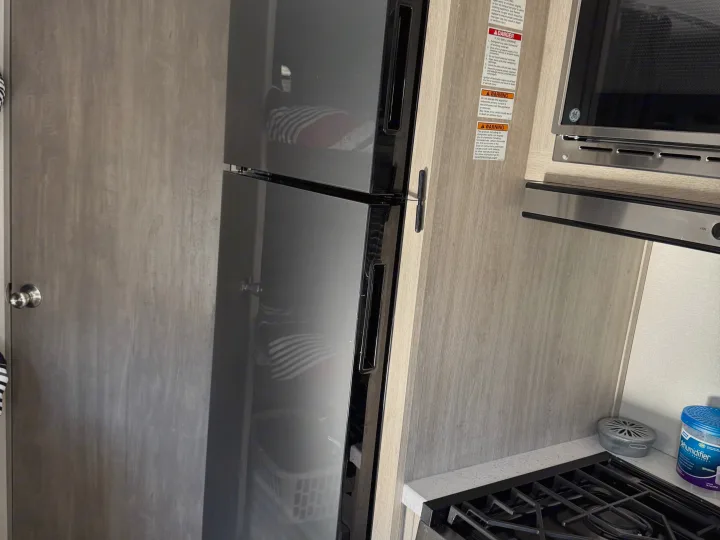 Compact RV rental kitchen interior with a dark refrigerator, GE microwave, stove, and warning labels on the wall.. Coachmen Catalina 261 bh 2026