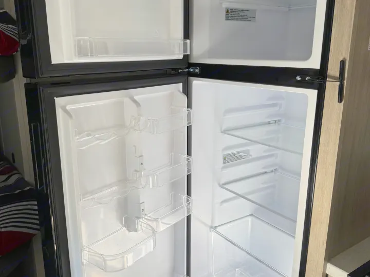 Clean, empty refrigerator inside an rv rental, showing shelves and door bins, ready for use.. Coachmen Catalina 261 bh 2026