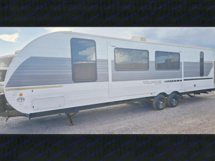 This white & grey Wildwood X-Lite travel trailer RV rental features multiple windows and is parked on gravel.. Forest River Wildwood X-Lite 2025