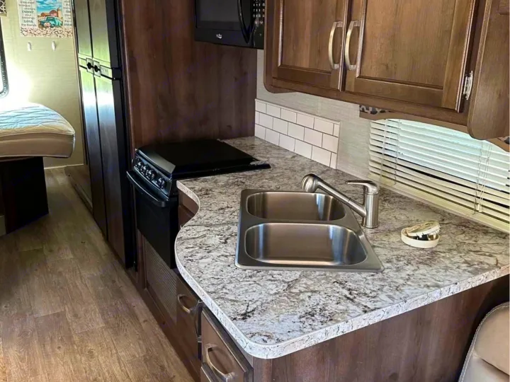 RV rental kitchen: modern double sink, stove, microwave, granite-look counters, wood cabinets, and practical storage.. Jayco Alante 2018