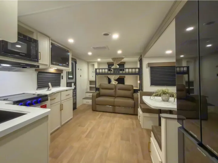 Clean, modern rv rental interior with a kitchen, dining booth, sofa, and bunk beds. Ideal for family travel.. Grand Design Transcend 2027