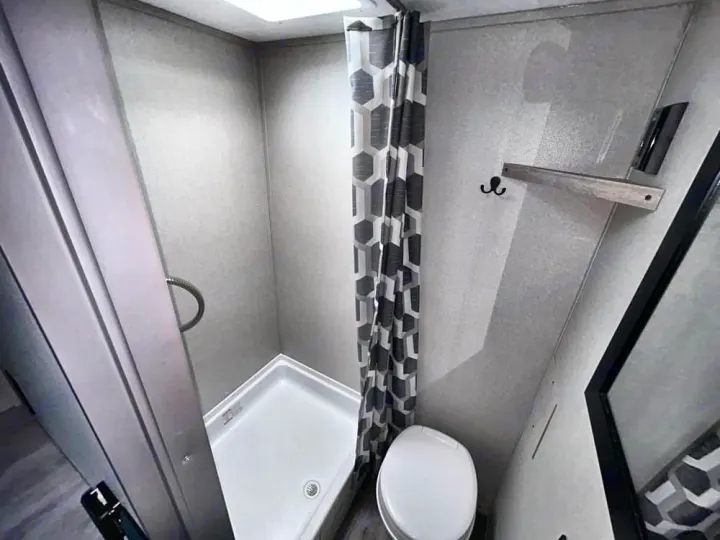 Compact RV rental bathroom features a shower, toilet, and geometric curtain, offering essential amenities for travel.. Coachmen Other 2024