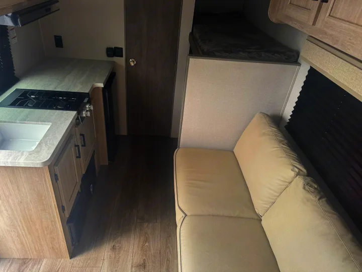 RV rental interior: A compact kitchen with stove and sink, a comfortable sofa, and an upper bunk bed.. Coachmen Other 2024