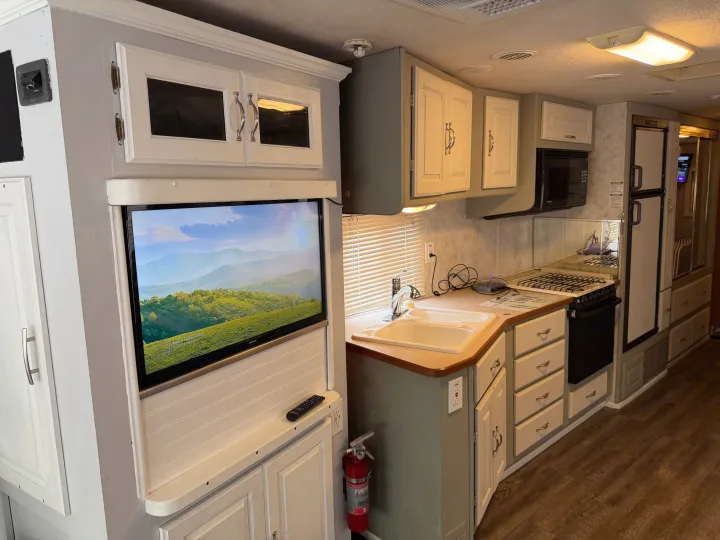 RV rental kitchen and living space, showing a TV, sink, stove, microwave, fridge, and ample storage cabinets.. Coachmen Cross Country 2003