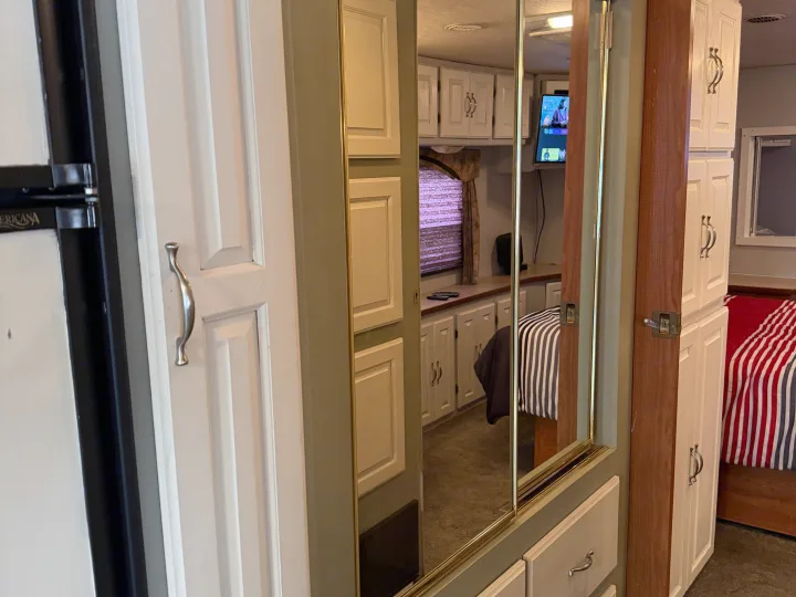 Cozy RV rental interior: a fridge on the left, mirrored closet reflecting a TV and bed, and white cabinets on the right.. Coachmen Cross Country 2003