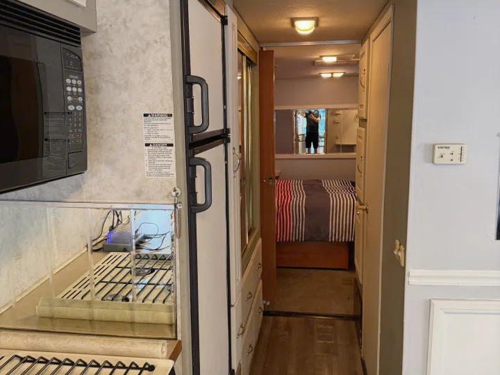 RV rental interior featuring a kitchen with microwave and refrigerator, hallway to a striped-bed bedroom. Safety labels included.. Coachmen Cross Country 2003
