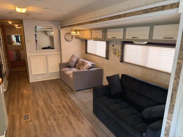 Spacious RV rental living area featuring two comfy sofas, wood-look flooring, overhead cabinets, and windows with blinds.. Coachmen Cross Country 2003