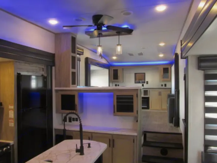 Spacious, modern rv rental interior: kitchen with island, fridge, blue accent lights, and steps to a living area.. Forest River Cherokee Arctic Wolf 2022