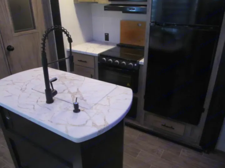 Modern RV rental kitchen featuring an island with a black faucet, white marble-look counters, stove, and refrigerator.. Forest River Cherokee Arctic Wolf 2022