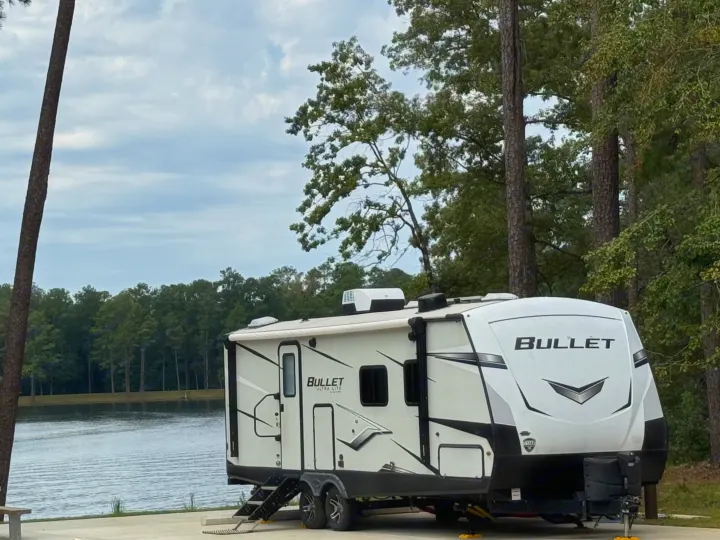 Enjoy nature in this beautiful RV rental, a "Bullet" trailer, parked by a lake, framed by tall trees.. Keystone RV Bullet Ultra Lite 2022