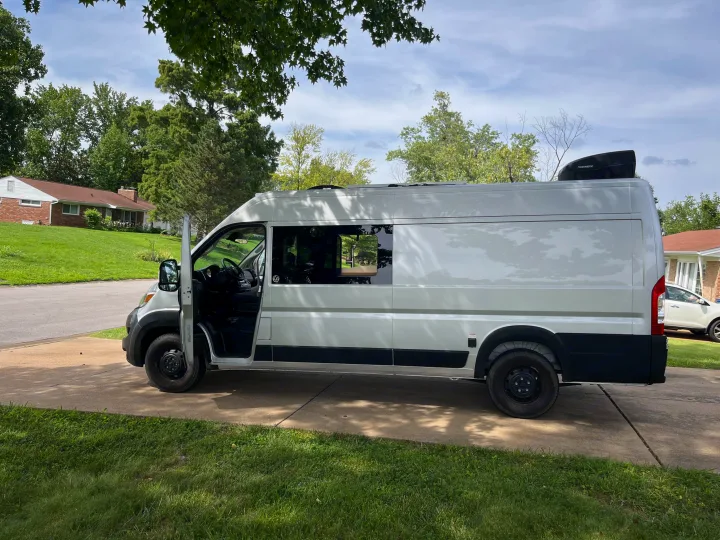 This bright white camper van, an excellent RV rental option, is parked on a suburban driveway with its door ajar, surrounded by greenery.. Dave & Matt Vans Dave & Matt Vans Class B 2023
