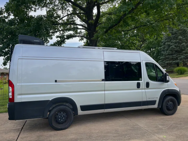 White "Dave & Matt Vans" RV rental camper van with Dometic AC & dark windows, parked on concrete among trees.. Dave & Matt Vans Dave & Matt Vans Class B 2023
