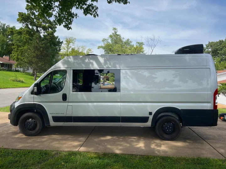 White "Dave & Matt Vans" RV rental parked on a driveway with trees. Features a window & Dometic unit on the roof.. Dave & Matt Vans Dave & Matt Vans Class B 2023