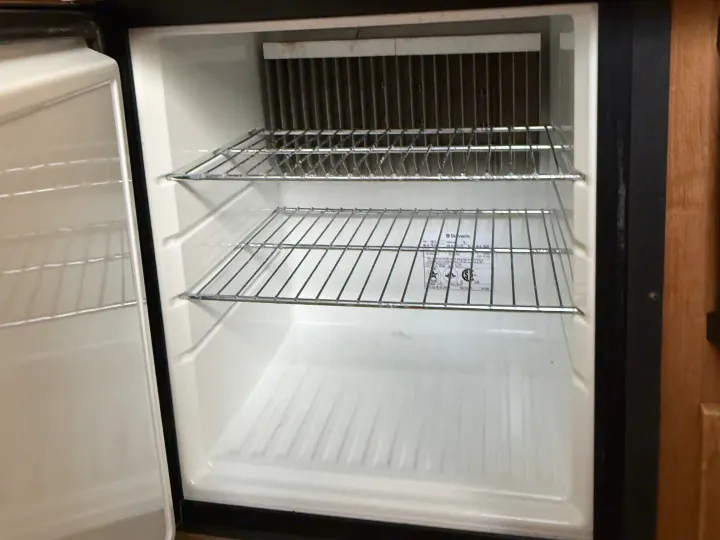 Clean, empty interior of an RV rental mini-fridge with wire shelves and a top freezer compartment, ready for use.. Forest River Rockwood Freedom 2013