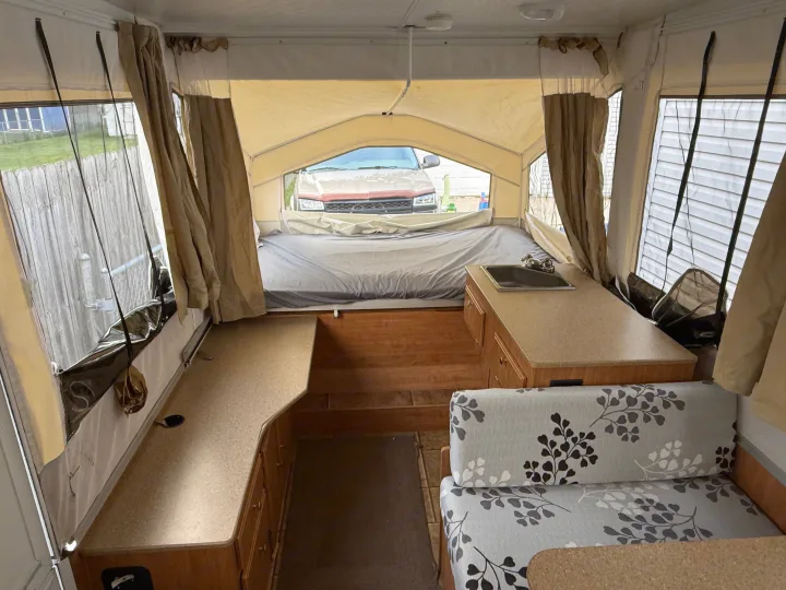 Explore this pop-up camper's interior for your rv rental! Bed, sink, counter, and floral cushions visible.. Forest River Rockwood Freedom 2013
