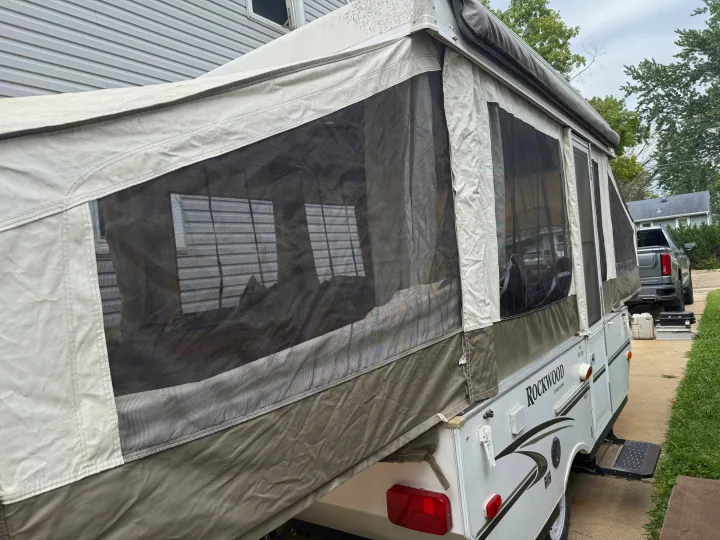 An extended pop-up camper rv rental, with its canvas and screens visible, parked on a driveway beside a house.. Forest River Rockwood Freedom 2013