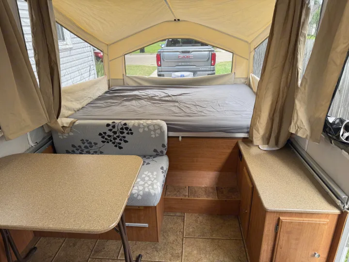 Inside a pop-up rv rental, showing a gray bed, patterned dinette, and bright exterior views through mesh windows.. Forest River Rockwood Freedom 2013