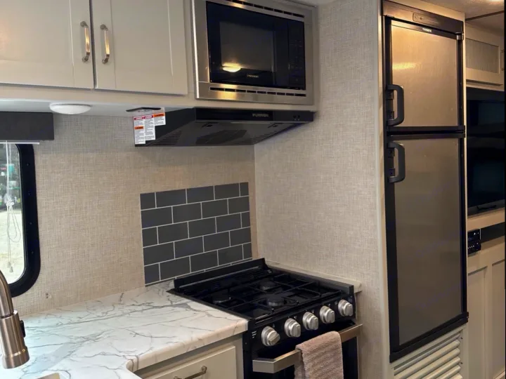 Modern RV rental kitchen with light cabinets, white marble-look counters, stove, microwave, and refrigerator.. Keystone RV Bullet Ultra Lite 2020