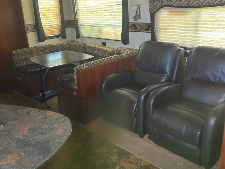 Interior of an RV rental: features a patterned dining booth, two comfy black recliners, and sunlit windows.. Crossroads RV Zinger 2012