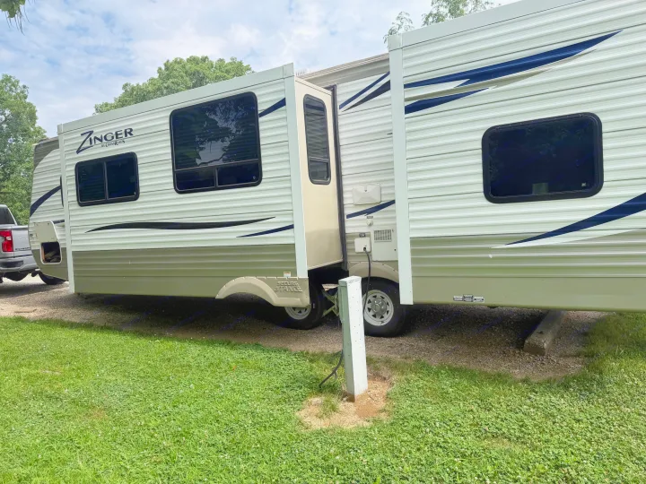 A Zinger travel trailer RV rental is parked at a gravel campsite with its side extended, ready for outdoor adventure.. Crossroads RV Zinger 2012