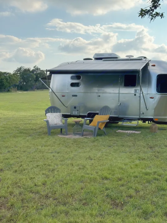 Enjoy your outdoor adventure! This Airstream RV rental includes a comfy lounge area with chairs and a table on a grassy field.. Airstream Caravel 2023
