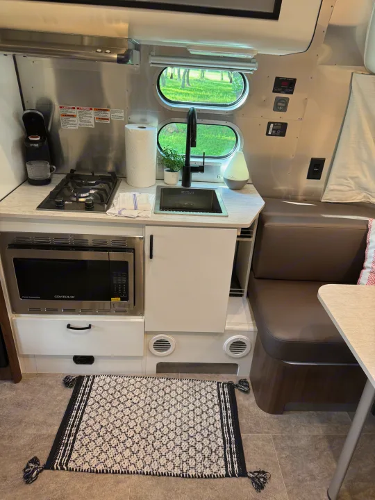 Modern RV rental: a compact kitchen with stove, sink, microwave, and adjacent dinette seating area.. Airstream Caravel 2023
