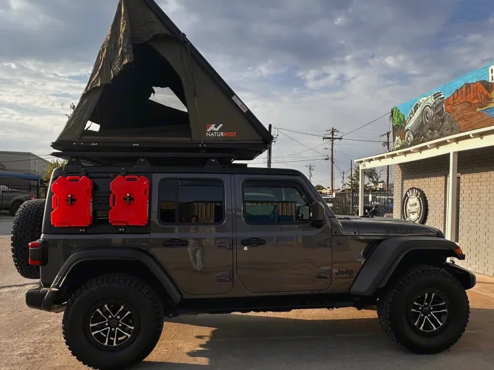 RV rental ready Jeep Wrangler featuring an open NaturNest rooftop tent, jerry cans, and rugged tires for off-roading adventures.. Jeep Wrangler 2024