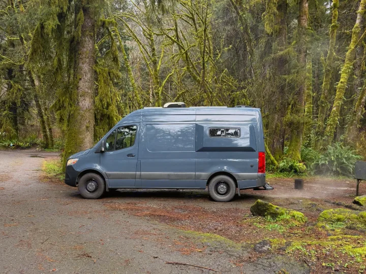 Gray rv rental camper van on a dirt road, surrounded by a lush, mossy forest. Ready for nature adventures.. Mercedes Sprinter 2500 2019