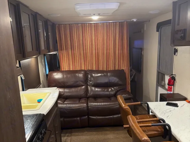 Cozy RV rental interior with a brown leather sofa, kitchen, dining area, and fire extinguisher near the door.. Forest River Salem Cruise Lite 2018