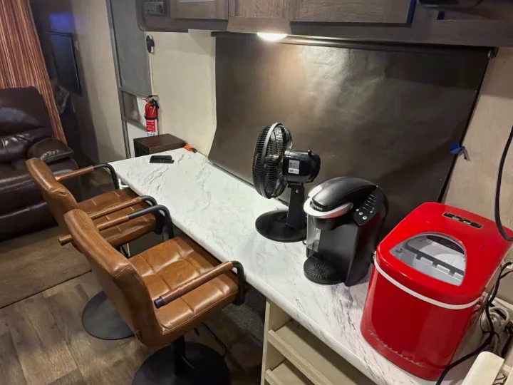 RV rental's compact interior: a white counter holds a Keurig, red ice maker, fan, and two brown bar stools.. Forest River Salem Cruise Lite 2018