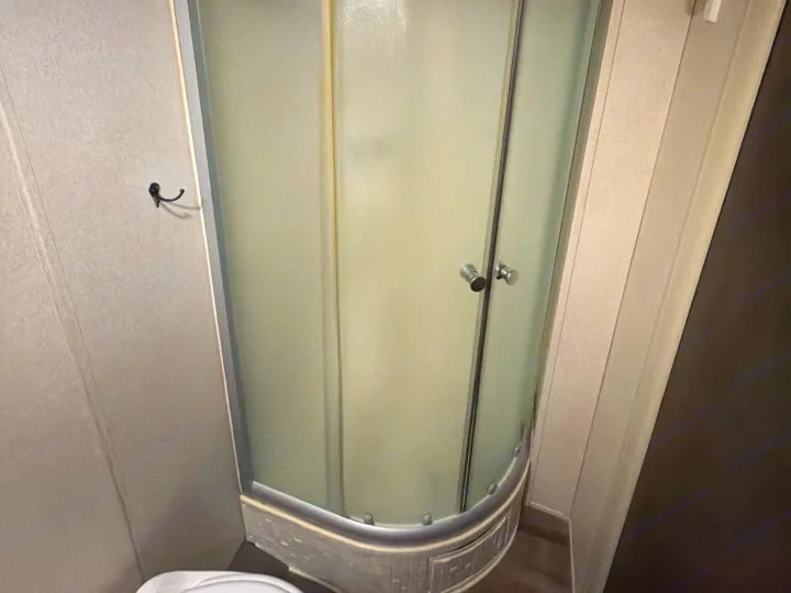 Inside an RV rental: a compact, frosted glass shower with a curved base. Features include metal trim and a wall-mounted hook.. Forest River Salem Cruise Lite 2018