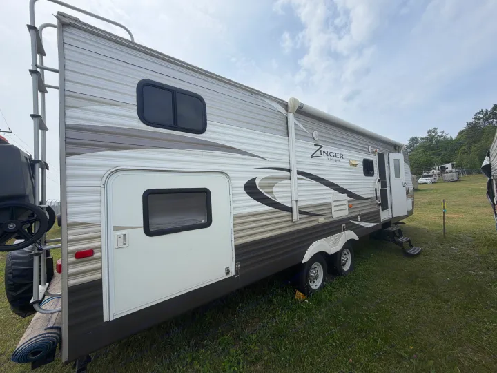A Zinger by Crossroads travel trailer RV rental, viewed from the side, with an awning, rear ladder, and entrance door.. Crossroads RV Zinger 2014