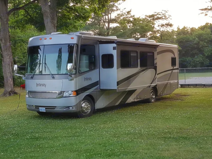 Spacious gray "Infinity" RV parked on a green campsite among tall trees. Perfect for your next rv rental adventure!. THOR Four Winds Infinity 2005