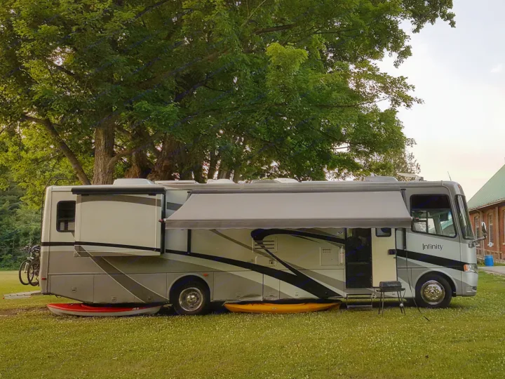 An RV rental with extended awning and kayaks parked on grassy field. A historic brick building stands in the background.. THOR Four Winds Infinity 2005