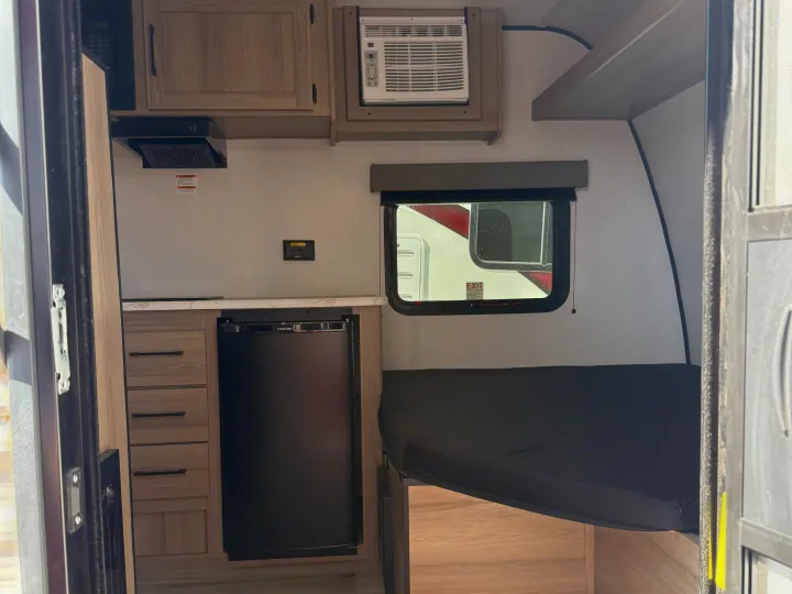 Compact RV rental interior: kitchen with microwave, fridge, AC unit, and a sleeping bunk. Ready for your next adventure!. Keystone RV Coleman 2026