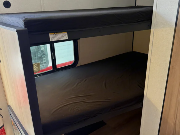 RV rental: Stacked bunk beds with dark mattresses. The top bunk has a 300 lbs warning label; a window is by the lower bed.. Keystone RV Coleman 2026