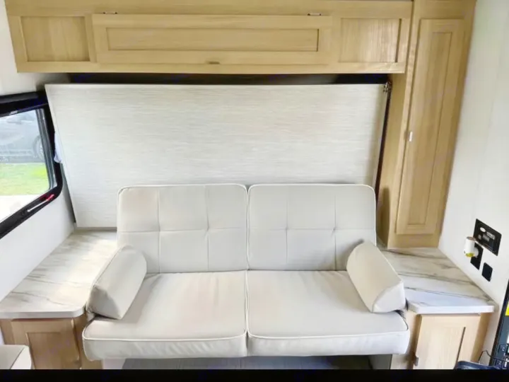 Modern RV rental interior: light-colored convertible sofa, overhead cabinets, and practical countertops maximize space for travel.. Forest River Wildwood FSX 2023