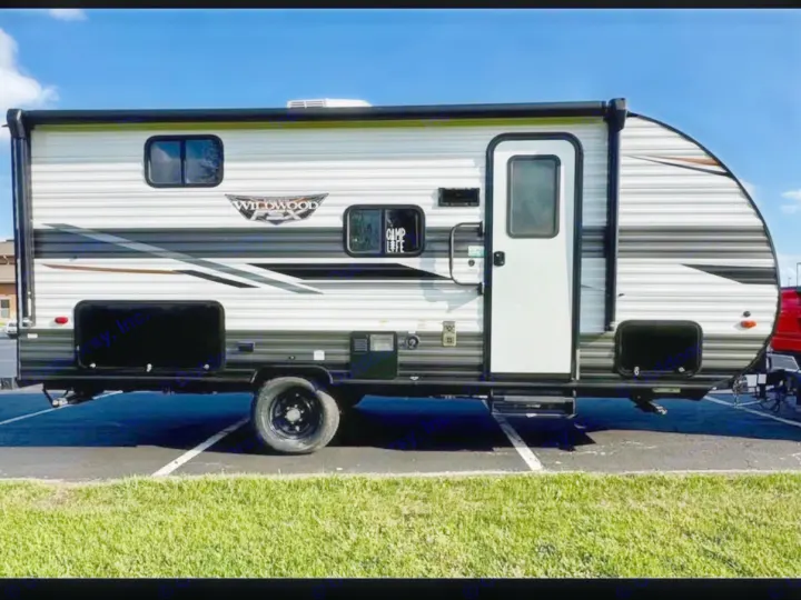 Side view of a white and gray Wildwood travel trailer, parked in a lot. An excellent option for your next rv rental.. Forest River Wildwood FSX 2023